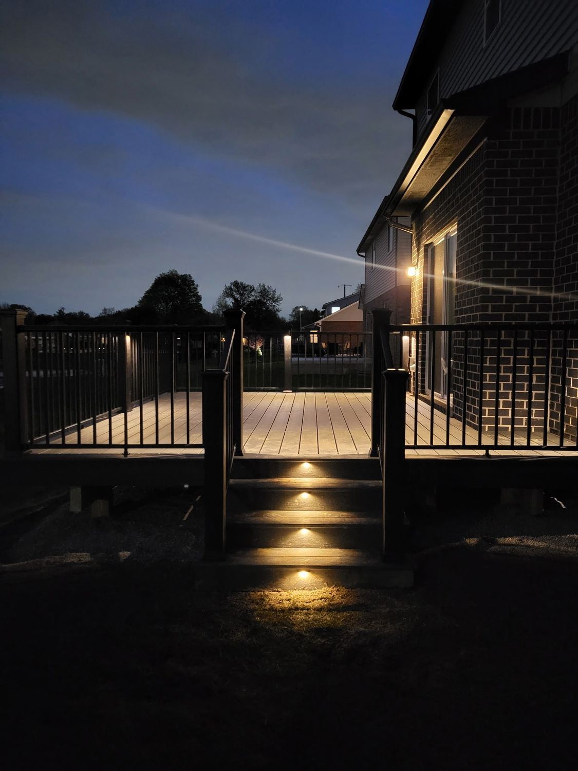 Trex Clamshell deck with black aluminum railing and glowing integrated step lighting at dusk